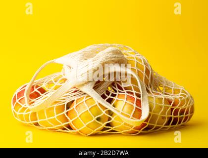 Null-Abfall-Konzept. Äpfel in einem Saitenbeutel auf gelbem Hintergrund. Keine Plastiktüten in Supermärkten und Geschäften. Stockfoto