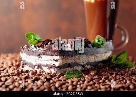 Köstlicher Schokoladenkuchen mit Minze und Kaffeegetränk mit Sahne. Kaffeebohnen sind auf dem Tisch verstreut. Kopierbereich. Stockfoto