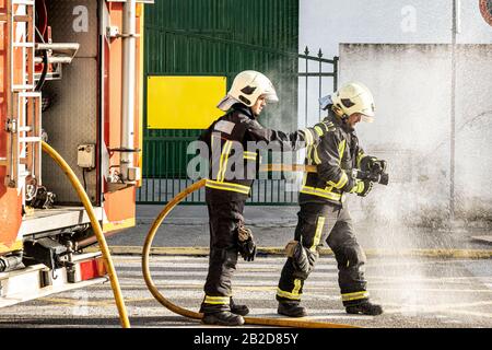 Feuerwehrleute mit einem Wasserschlauch, der Wasser zieht, um einen Brand auszusetzen Stockfoto