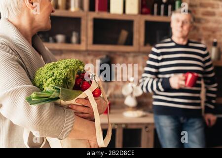 Älteres Paar Auspacken von Öko-Tüten mit biologischem Gemüse in der Küche Stockfoto
