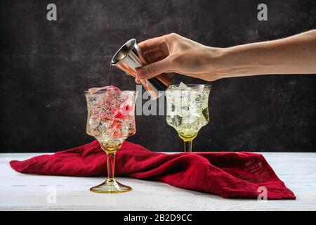 Hand von Barkeeper mit Zigger, der Granatapfenbitter in Cocktail mit Gin gießt Stockfoto