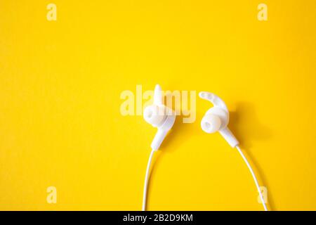 Weiße Kopfhörer mit Kabelanschluss auf gelbem Hintergrund. Buntes Frühlings-Konzept. Stockfoto