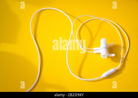 Weiße Kopfhörer mit Kabelanschluss auf gelbem Hintergrund. Buntes Frühlings-Konzept. Stockfoto