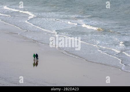 Ein älteres oder mittleres Paar, das Arm in Arm entlang eines menschenleeren Strandes an der norfolkküste geht Stockfoto