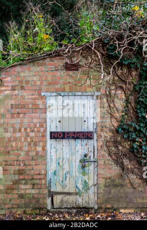 Eine alte Holztür im schäbigen, rustikalen, verwitterten Stil in einer Gartenmauer in einem ummauerten Garten. Stockfoto