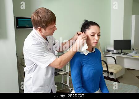 Aufmerksamer, entgeltlicher Arzt, der eine hübsche Frau auf Ohrenprüfung macht Stockfoto