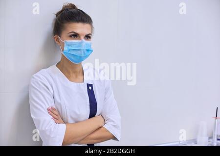 Junge, ernsthafte, selbstbewusste Frau, Ärztin in medizinischer Maske mit gefalteten Armen Stockfoto