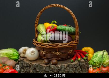 Frisches Gemüse in einem Weidenkorb auf einem Stumpf mit schwarzem Hintergrund und Kopfformchen. Stockfoto