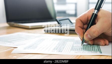 Abschluss des US-Steuerformulars 1040 und manuelle Berechnung und Befüllung von Berichtspapieren mit Laptop im Büro. Stockfoto