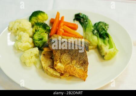 In der Pfanne gebratenes Seebarschfilet mit Kartoffelpüree und gedünstetem Gemüse Stockfoto