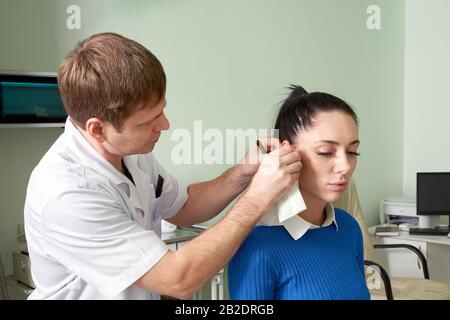 Aufmerksamer, entgeltlicher Arzt, der eine hübsche Frau auf Ohrenprüfung macht Stockfoto