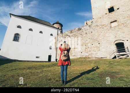 Stara Lubovna, Slowakei - Dezember 2019: Frau im roten Mantel, die sich mit der Burgruine Lubovniansky Hrad fotografiert. Stockfoto