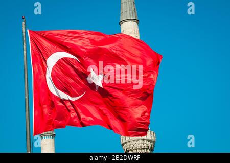 Türkische Flagge vor einem Moschee-Minarett unter sonnenblauem Himmel in Istanbul, Türkei Stockfoto