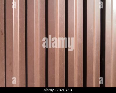 Blick auf ein gewelltes braunes Eisenblech mit senkrechten Wellen, die bei hellem Sonnenlicht von der Seite beleuchtet werden. Der Kontrast von Licht und Schatten. Stockfoto