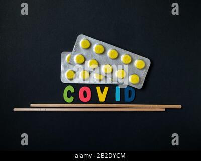 Blasen mit gelben Pillen, die Aufschrift bezeichnet einen Virus und asiatische Essstäbchen auf schwarzem Grund. Symbol von Leckereien aus Asien in Form von Co Stockfoto