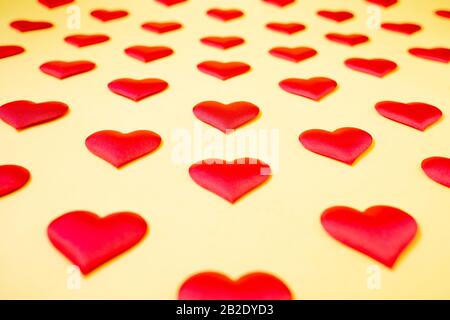 Viele identische rote Seidenherzen liegen versetzt auf gelbem Grund. Symbol für Liebe, Zärtlichkeit und Leidenschaft. Stockfoto