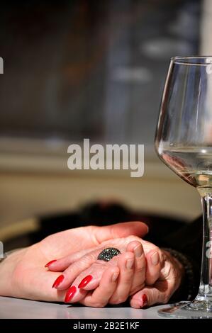 Ältere Mutter hält die Hand der Tochter auf einem Restauranttisch mit einem Glas Weißwein daneben. Tageszeitteilungmit der Mutter. Hände halten Stockfoto