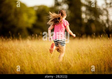 Junges Mädchen, das durch ein überwachsenes Rasenfeld läuft Stockfoto