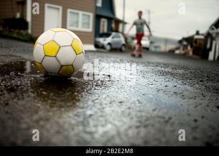 Junge, der mit einem Fußballball auf der Straße spielt Stockfoto