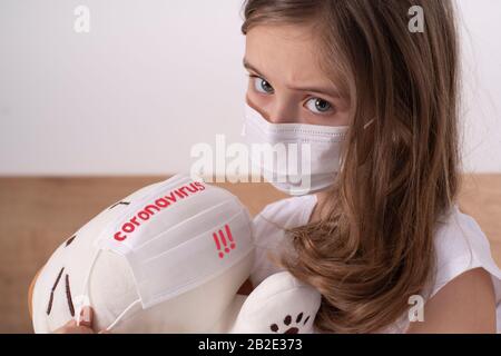Das Mädchen ist traurig wegen des Virus.Kleines trauriges Mädchen in einem weißen T-Shirt in einer Schutzmaske spielt mit einem Spielzeug.Konzept des Kampfes gegen Coronovirus Stockfoto