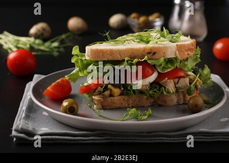 Sandwich mit Huhn, Kirschtomaten, Wachteleiern, Oliven und Mikrogrüns vor dunklem Hintergrund Stockfoto