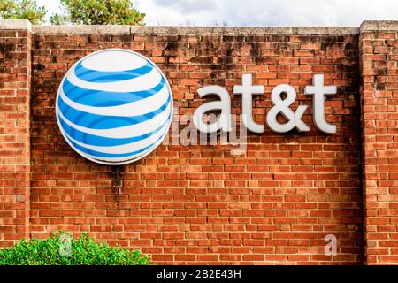 Charlotte, NC/USA - 14. Dezember 2019: Mittlerer horizontaler Schuss von Marke "AT&T" und Logo auf einer roten Ziegelwand mit Bäumen, geparkten Autos und Sturm c Stockfoto