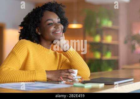 Begeisterte Afro-Mädchen träumen von einer wohlhabenden Zukunft und trinken Tee Stockfoto