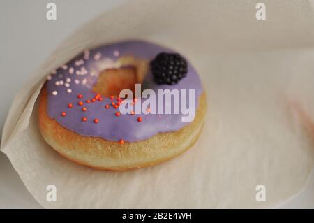 Ein Donut mit lila Creme, Süßigkeiten und Beeren in Backpapier Stockfoto