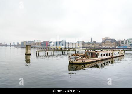 Altes rostig sinkendes Abandonboot in der Nähe von Pier an der Spree im Treptow Bezirk, in Berlin, Deutschland im Winter mit bewölktem Himmel. Stockfoto