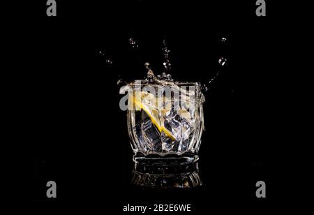Aqua-Wasser mit Zitronensoda verschüttet, wenn Eis mit Tropfen auf einen schwarzen Backgroun geworfen wird Stockfoto