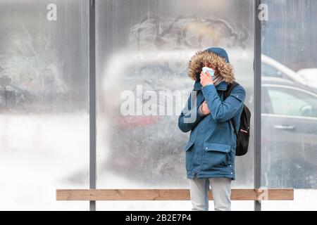 Kranker Mann mit einer Haube allein auf öffentlichen Verkehrsmitteln hält an, hustet, trägt eine schützende Gesichtsmaske gegen übertragbare Infektionskrankheiten und schützt Stockfoto