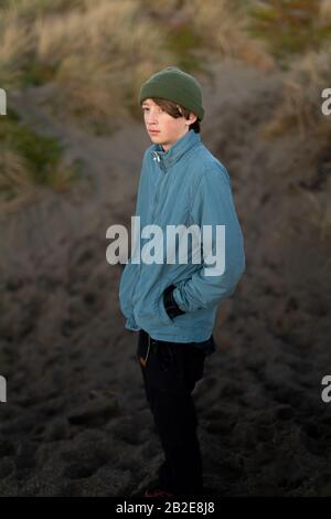 Teenager-Junge, der in der Dämmerung am Fuße einer Düne an der Küste steht Stockfoto