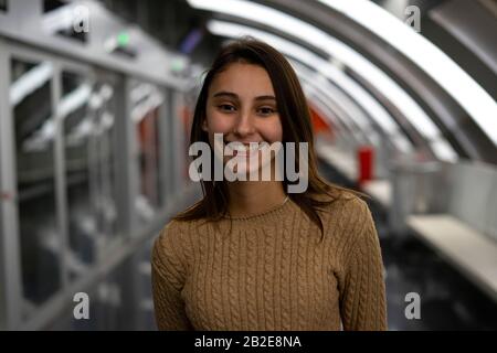 Junge und schöne Frau lächelt in einer modernen Metrostation. Konzept des Verkehrs und der U-Bahn. Stockfoto