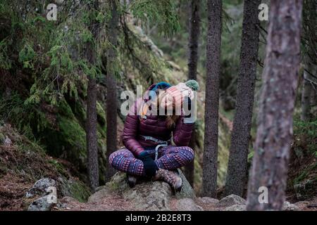 Frau, die auf einem Felsen sitzt und den Kopf in den Händen hält, während sie alleine wandert Stockfoto