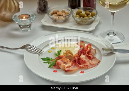 Warmer Ziegenkäse mit Honig und Speck auf einem weißen Gericht, serviert mit einem Glas köstlichen Weißweins. Stockfoto