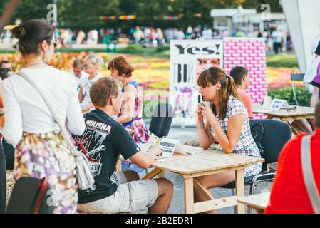 Moskau, Russland - 9. August 2014. Junge Frau und ein Mann sitzen einander gegenüber auf einem Holztisch und kommunizieren miteinander. Schnelle Terminveranstaltung in der Sololniki Stockfoto