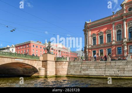 Blick von einem Kanal mit elektrischen und Telefonkabeln über die Anichkow-Brücke und die Pferdetamer-Skulptur in Sankt Petersburg, Russland. Stockfoto