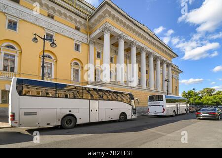 Unbeschreiblich weiße Reisebusse fahren vor einem farbenfrohen Regierungsgebäude in Sankt Petersburg, Russland. Stockfoto