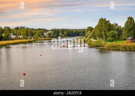 Ein farbenfroher Himmel, während die Sonne über Boote, Dock, Häuser und einen Park entlang des Porvoonjoki-Flusses in Porvoo, Finnland untergeht. Stockfoto