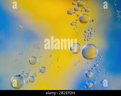 Öl fällt auf Wasser mit gelbem und blauem Hintergrund Stockfoto