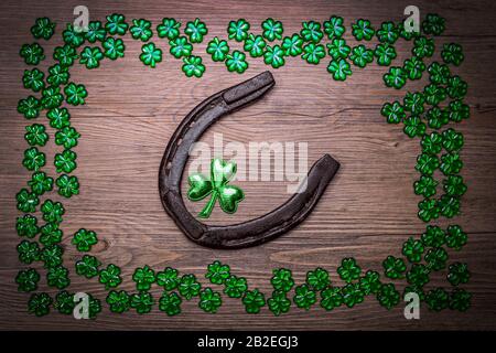 Hintergrund mit rostigen Hufeisen, Shamrocks über rustikalem Holz. St. Patrick's Day Feriensymbol. Glücksbringer. Draufsicht, Kopierbereich. Stockfoto