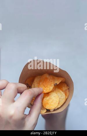 Frau, die einen Papierkegel voller Kartoffelchips hält. Draufsicht. Ansicht von oben Stockfoto