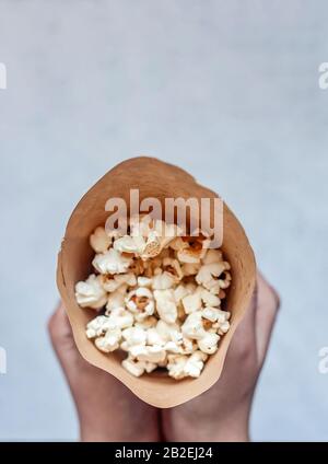 Frau, die einen Papierkegel voller Popcorn hält. Draufsicht. Ansicht von oben Stockfoto