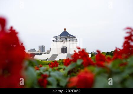 (Selektiver Fokus) Atemberaubender Blick auf die Nationale Chiang Kai-shek Gedenkhalle im Hintergrund und verschwommene rote Blumen im Vordergrund. Stockfoto