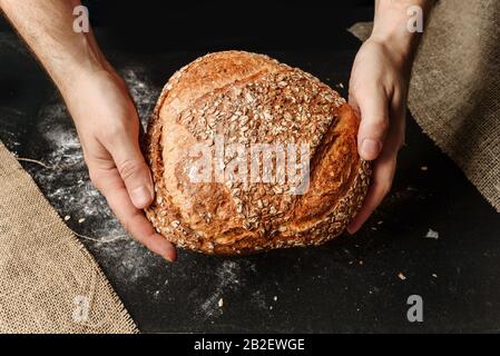 Ein Mann hält in seinen Händen einen Laib von rustikalem Biobrot. Das Konzept einer ländlichen Bäckerei. Stockfoto