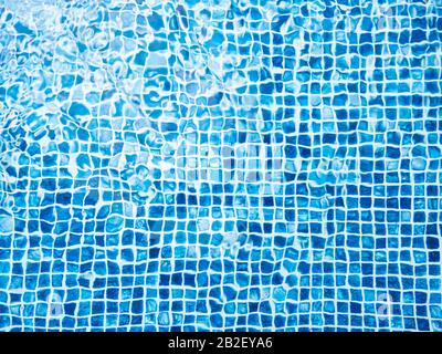 Das Licht, das auf der Oberseite der Wasseroberfläche des Pools reflektiert wurde, war unten mit blauen Mosaikfliesen ausgekleidet. Das Wasser wellt sich auf der Rückseite des blau gefliesten Schwimmbads Stockfoto