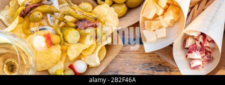 Tapas und Pinchos Panorama mit Weißwein. Käse, Jamon, gildas, Oliven auf einem Holztisch in einem Café im Freien, von oben geschossen Stockfoto