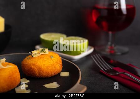 Hausgemachte Kroketten, gefüllt mit Käse mit Zitrone und einem Glas Rotwein. Stockfoto