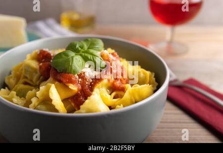 Hausgemachtes Dinner Tortellini mit Tomatensauce arrabbiata und Käse mit einem Glas Wein auf der Seite. Stockfoto