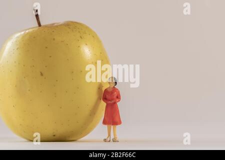 Miniaturfigur der Frau neben dem großen gelben apfel stehend. Geringe Tiefe des Feldhintergrunds. Gesundheitswesen, gesunder Lebensstil und schlankes Konzept. Stockfoto